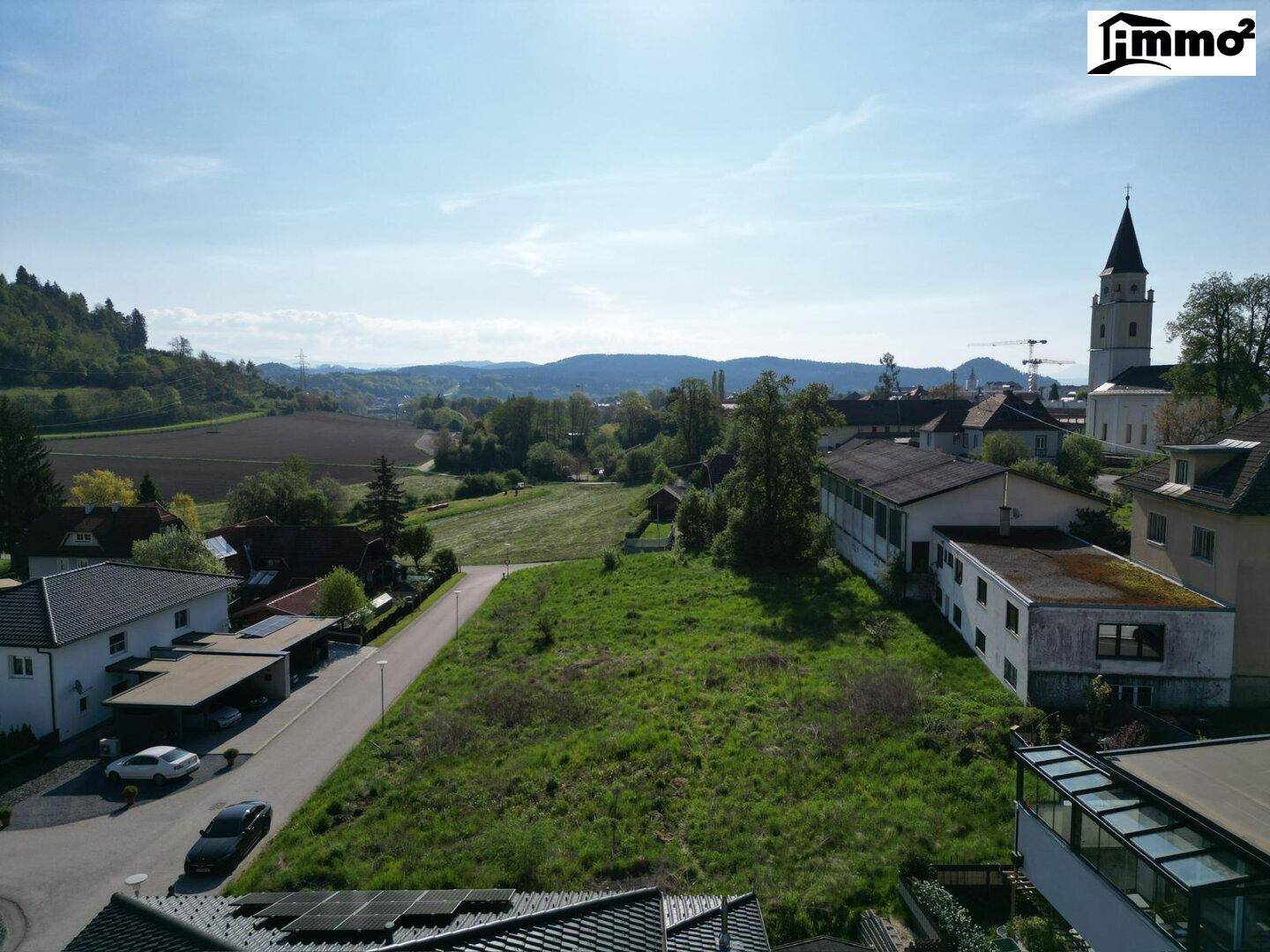 Weitläufige Ansicht eines Grundstücks mit angrenzenden Häusern und einem Kirchturm in der Ferne.