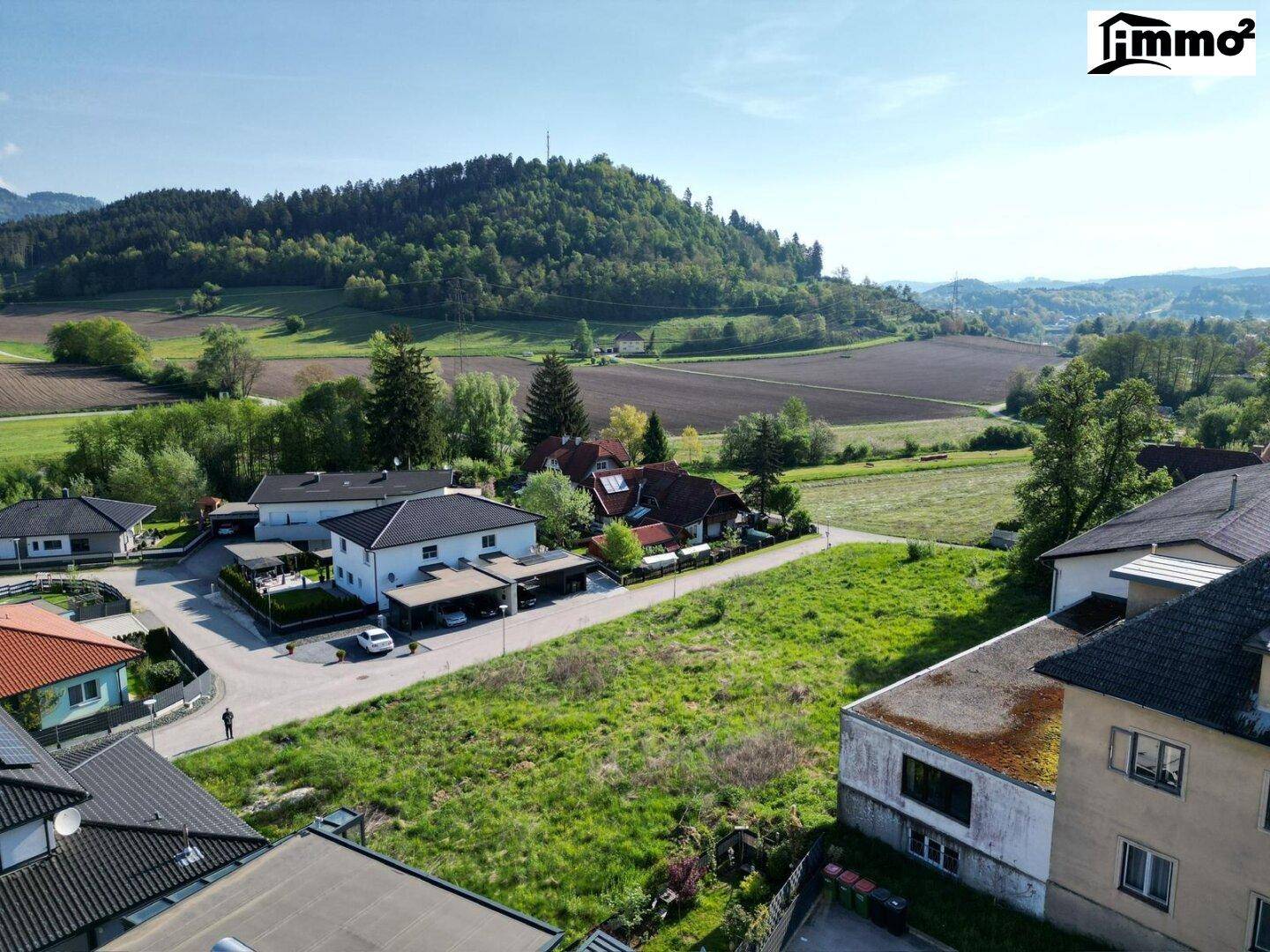 Panoramablick auf ein grünes Baugrundstück, umgeben von Einfamilienhäusern und ländlicher Umgebung.