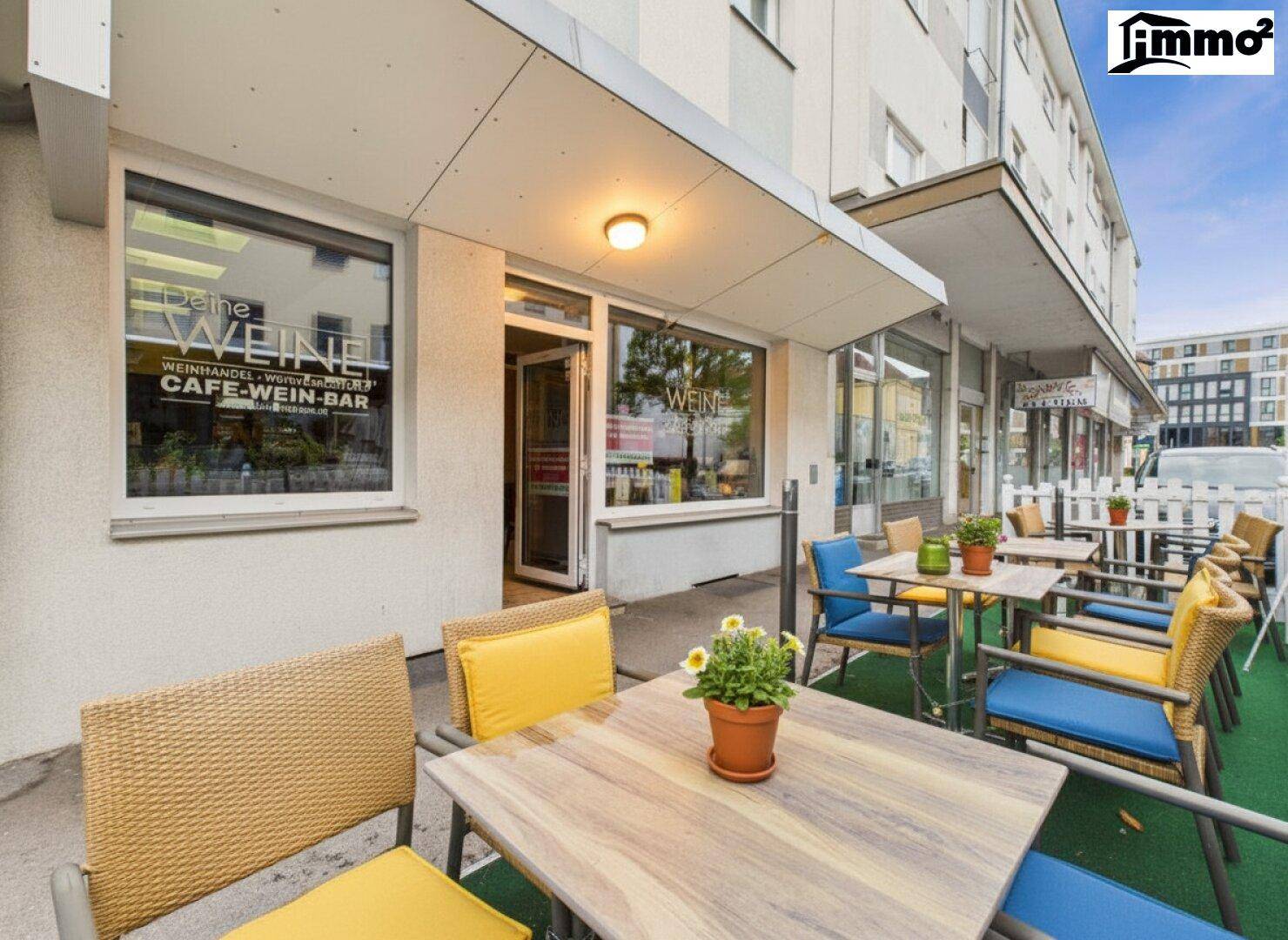 Eingangsbereich des Cafés mit Außenterrasse und Werbeschildern an den Fenstern.