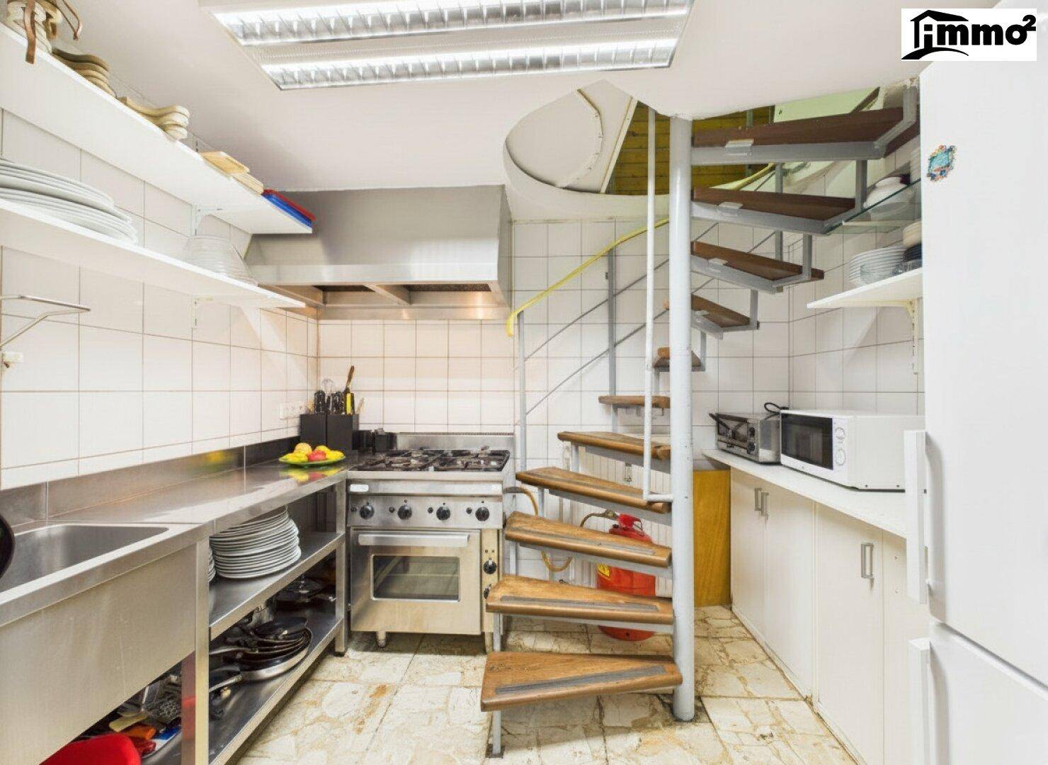 Professionelle Küche mit Edelstahlgeräten, Gasherd und einer Wendeltreppe.