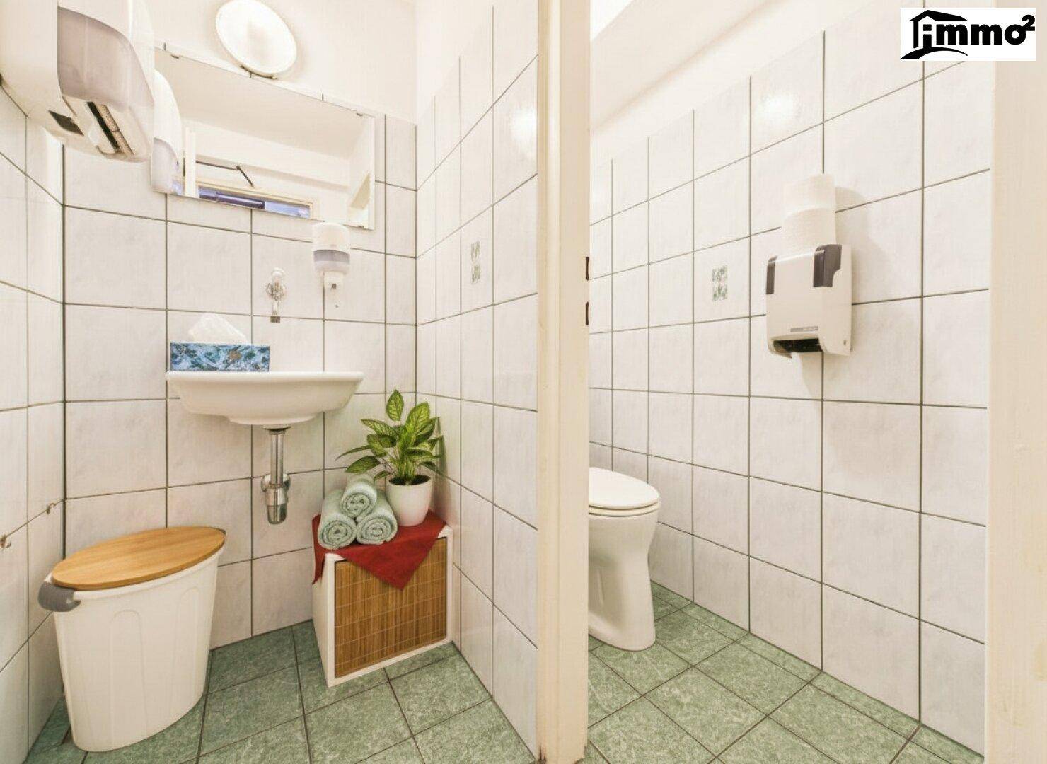 Einfache Toilette mit Waschbecken, Spiegel und grünen Bodenfliesen.
