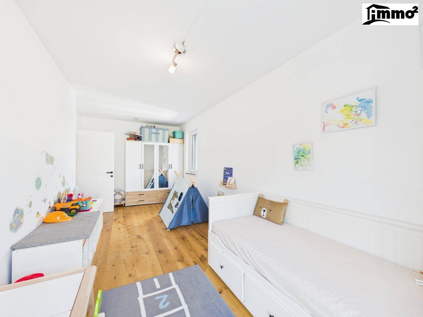 Freundliches Kinderzimmer mit Holzboden, Spielzeug und weißem Kleiderschrank.