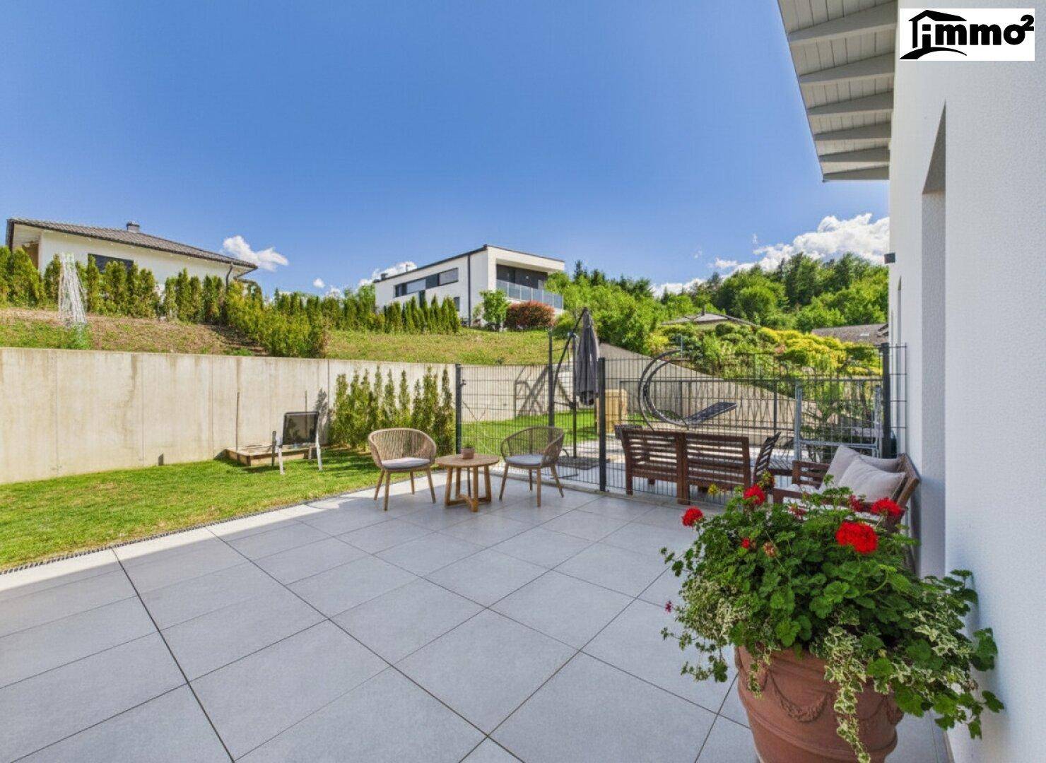Große geflieste Terrasse mit Gartenmöbeln und angrenzender Rasenfläche.