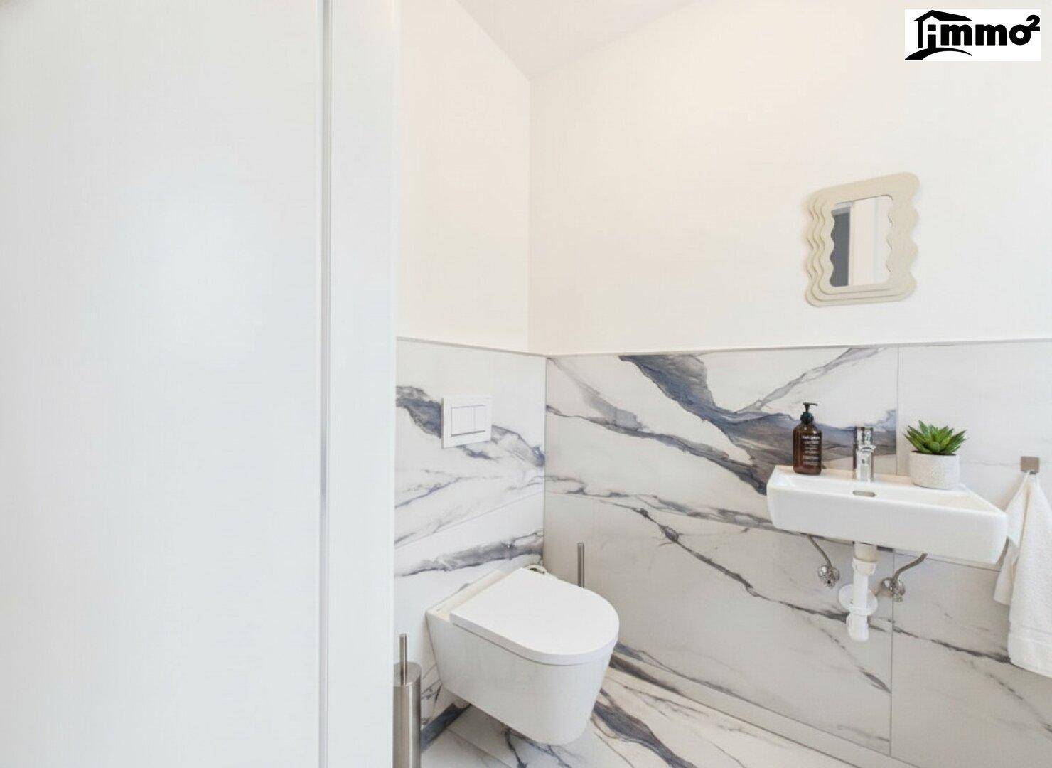 Modernes Gäste-WC mit Marmorfliesen, wandhängendem WC und kleinem Waschbecken.
