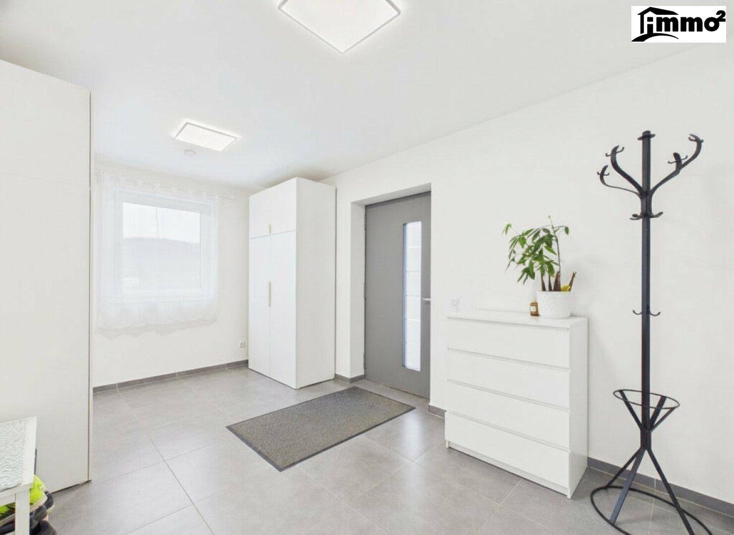 Heller Eingangsbereich mit Fliesenboden, Garderobe und weißer Kommode.