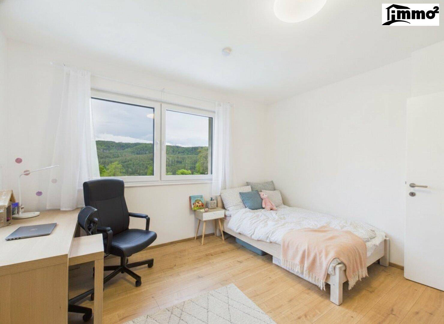Helles Schlafzimmer mit Holzboden, Schreibtisch und Fenster mit Blick ins Grüne.