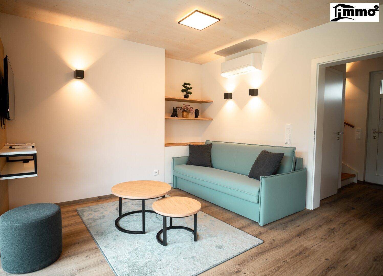 Gemütlicher Wohnbereich mit mintgrünem Sofa, Holztischen und indirekter Beleuchtung.