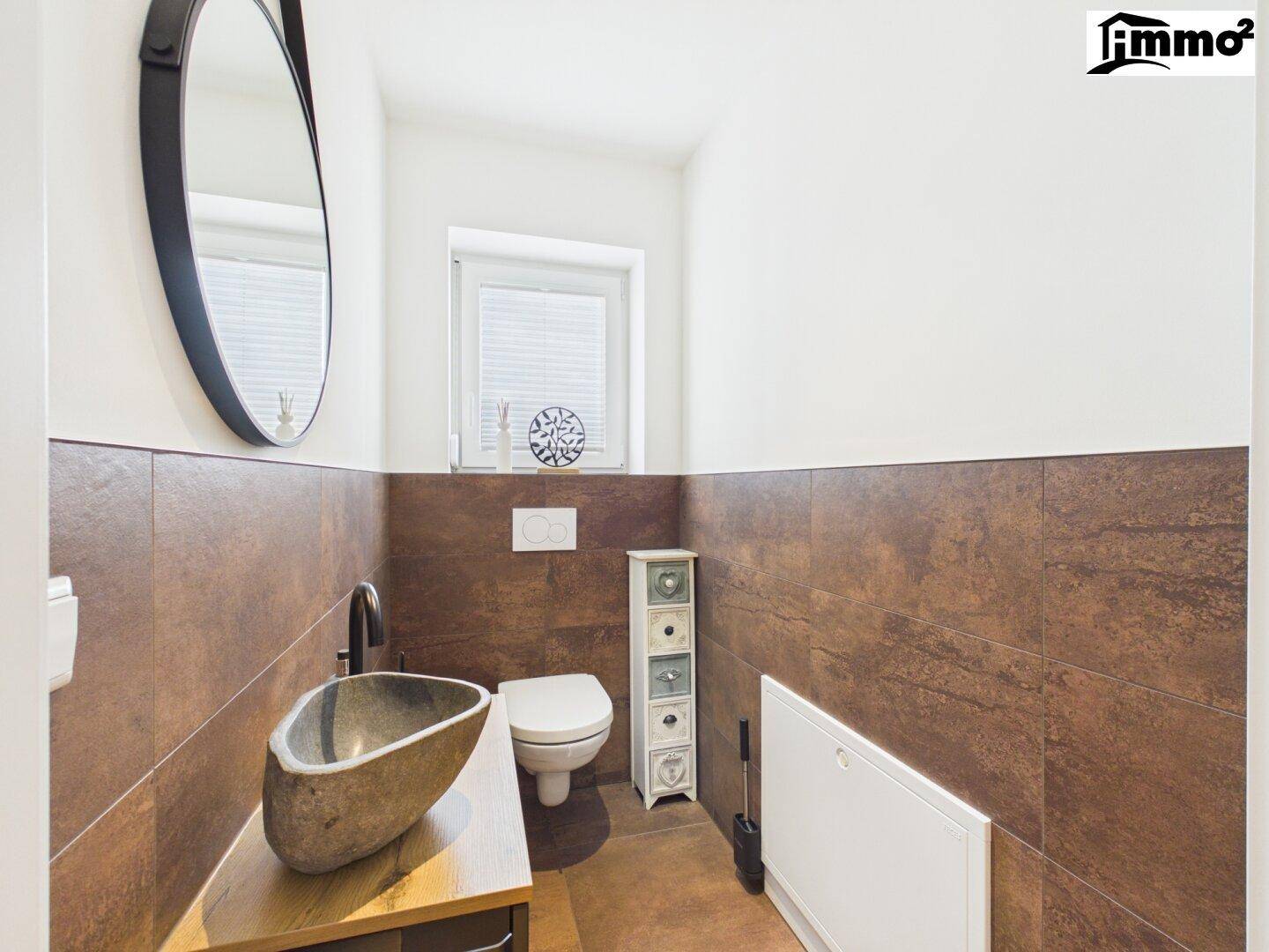 Modernes Gäste-WC mit Steinwaschbecken, Wand-WC und braunen Fliesen an den Wänden.