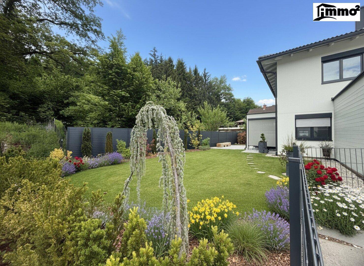 Idyllischer Gartenbereich mit vielfältigen Pflanzen, Rasen und einem modernen Zaun.