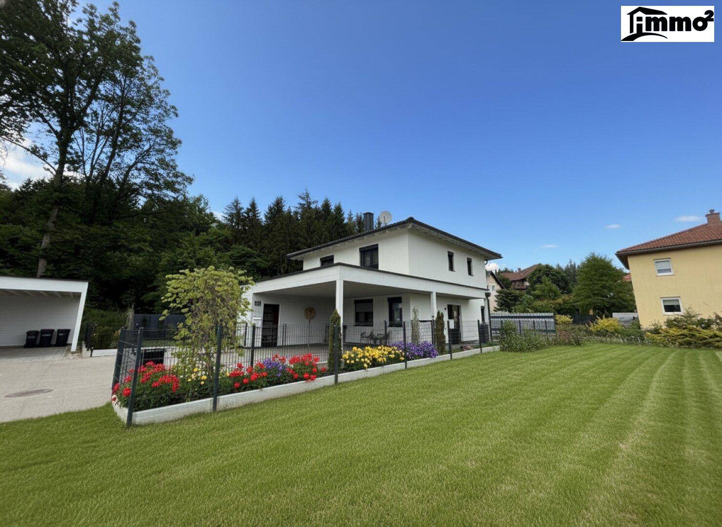 Gepflegter Garten mit Rasenfläche, Blumenbeeten und einem modernen Einfamilienhaus im Hintergrund.
