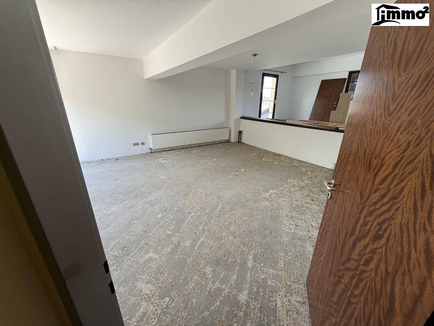 Leerer Raum mit abgenutztem Bodenbelag und weißen Wänden, bereit für Renovierung.