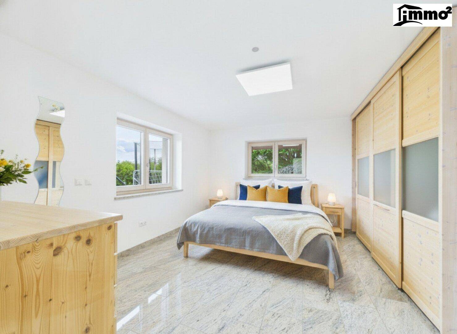 Helles Schlafzimmer mit Holzbett, Einbauschränken und zwei Fenstern mit Blick ins Grüne.