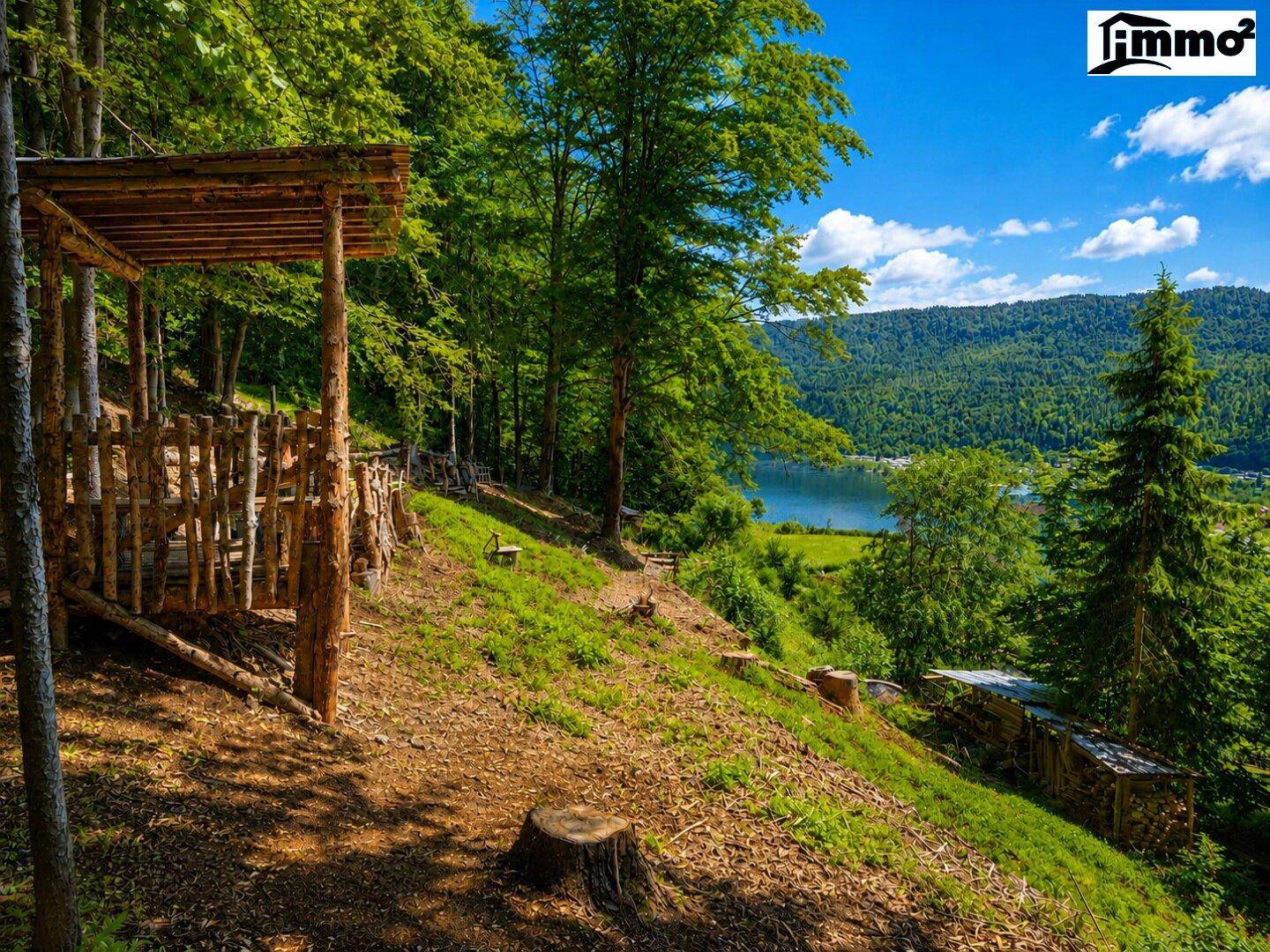 Idyllische Naturlandschaft mit Wald, See und rustikalem Holzunterstand unter blauem Himmel.