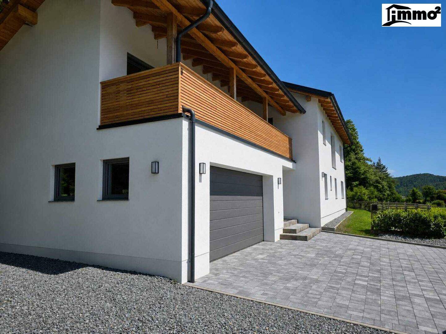 Ansicht des modernen Hauses von der Seite mit Garage, Balkon und gepflasterter Auffahrt.