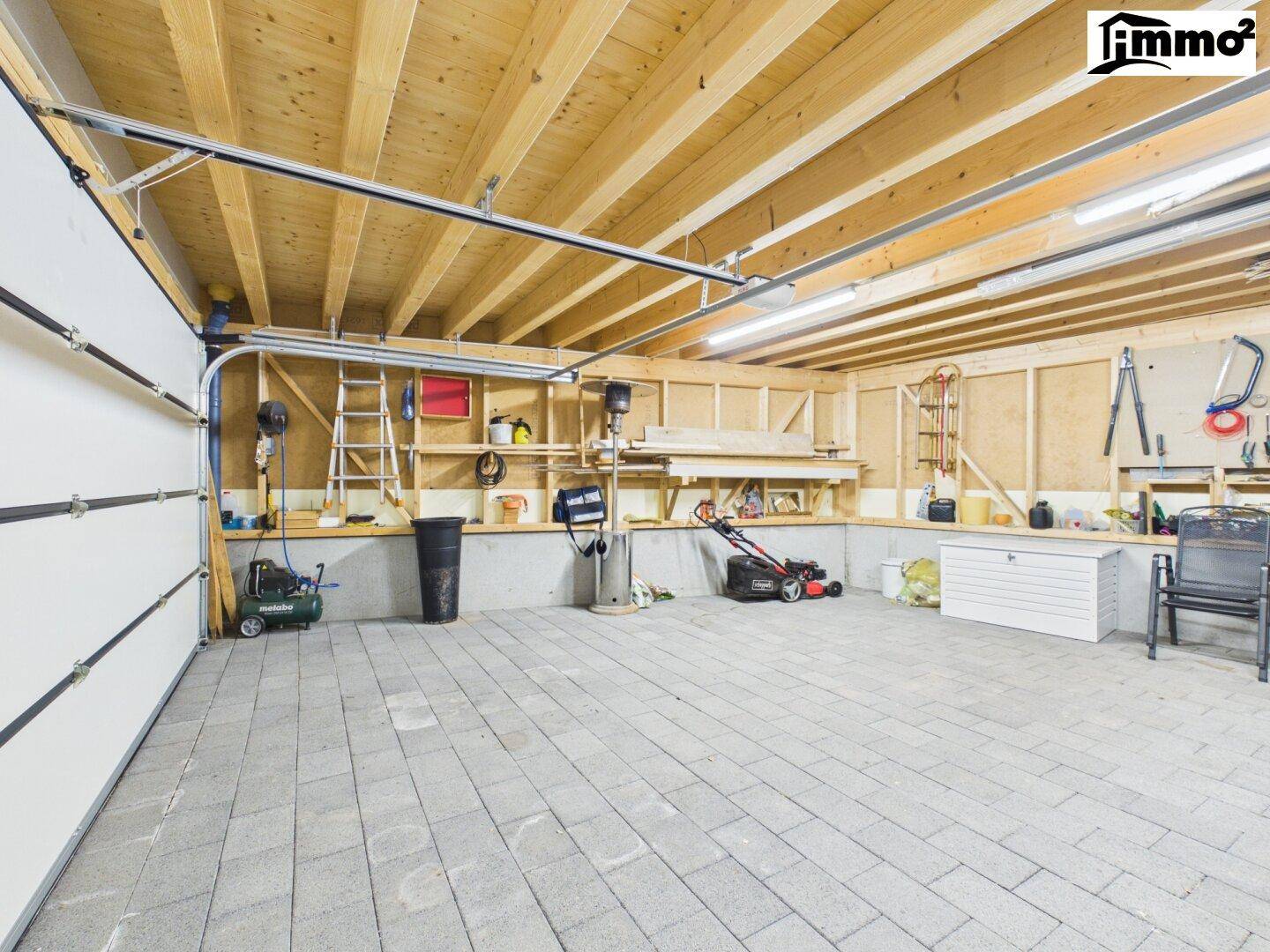 Geräumige Garage mit Betonpflasterboden, Holzdecke und viel Stauraum für Werkzeuge.