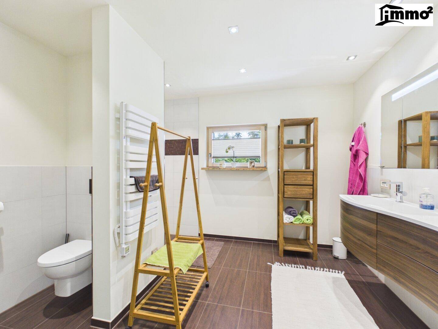 Modernes Badezimmer mit dunklen Fliesen, Holzwaschtisch, WC und beheiztem Handtuchhalter.
