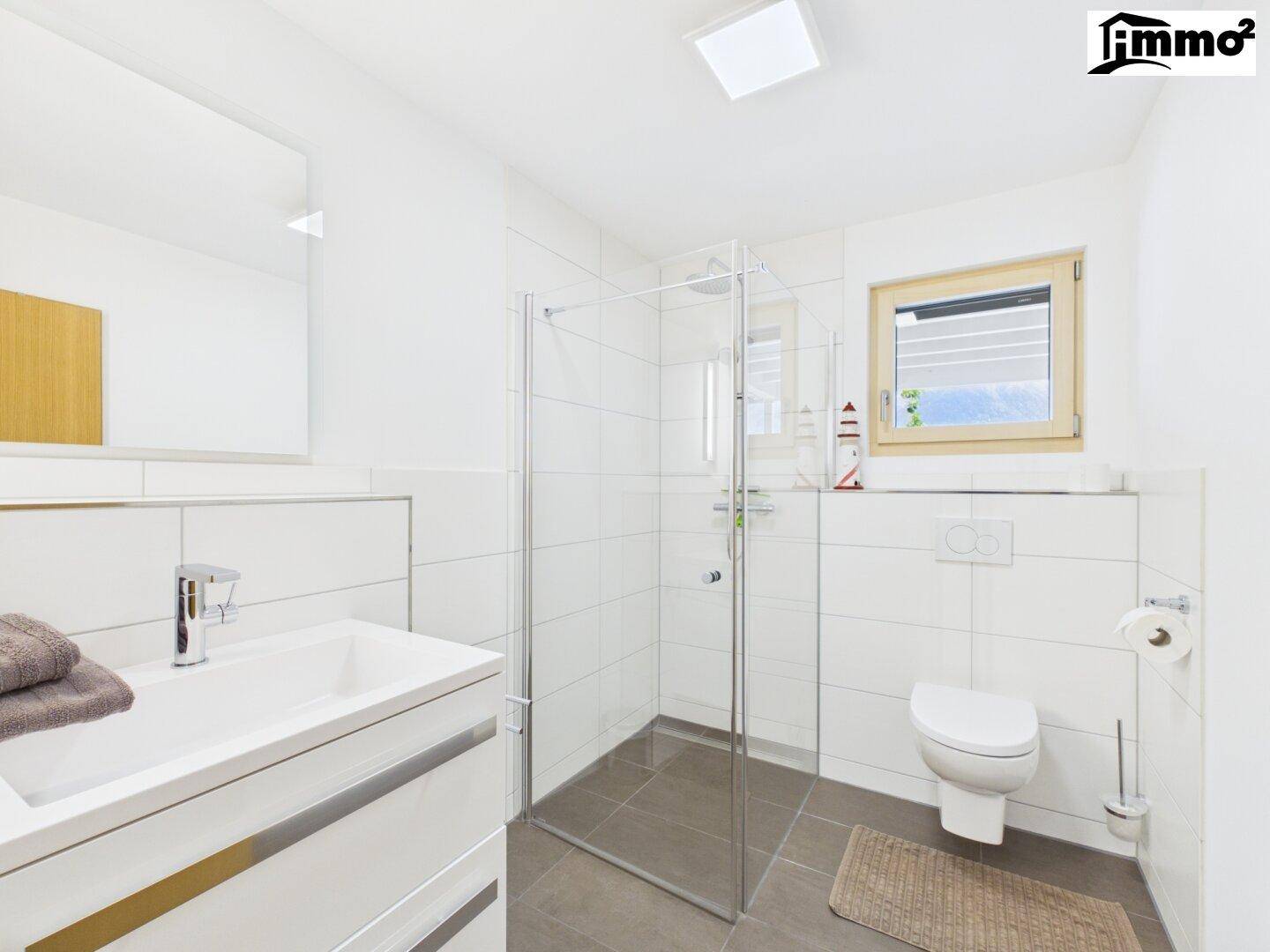 Modernes Badezimmer mit Duschkabine, WC, Waschtisch und Fenster für Tageslicht.