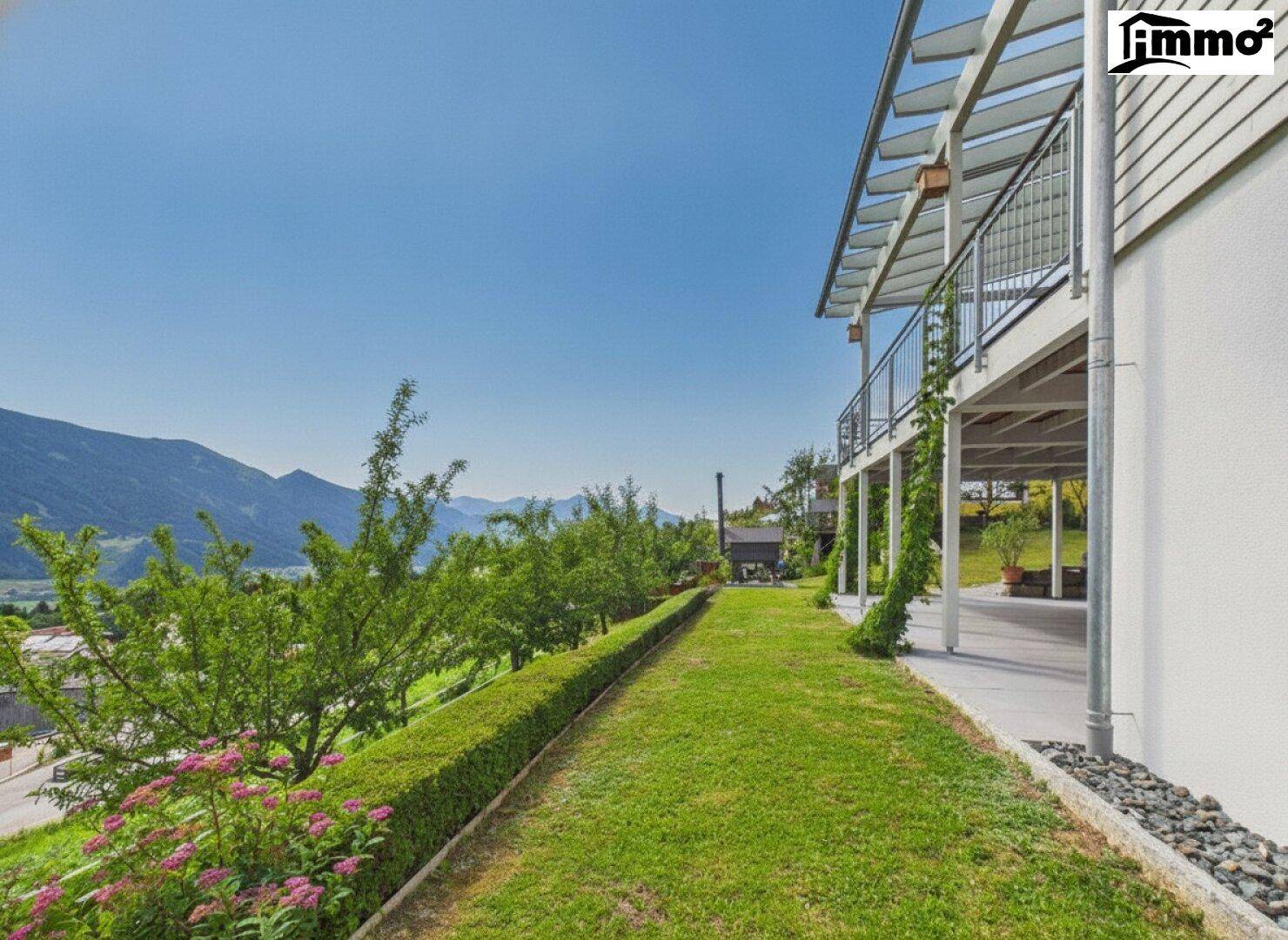 Gepflegter Gartenbereich mit Rasenfläche und Hecke entlang des Hauses, mit Bergblick im Hintergrund.