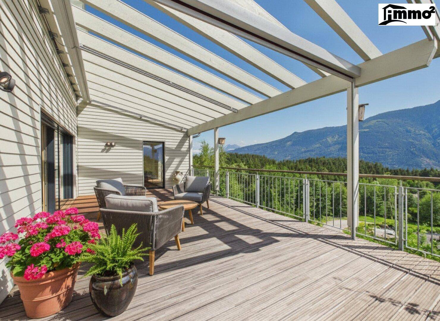 Große Holzterrasse mit bequemen Loungemöbeln und weitem Blick auf die Berge und die grüne Umgebung.