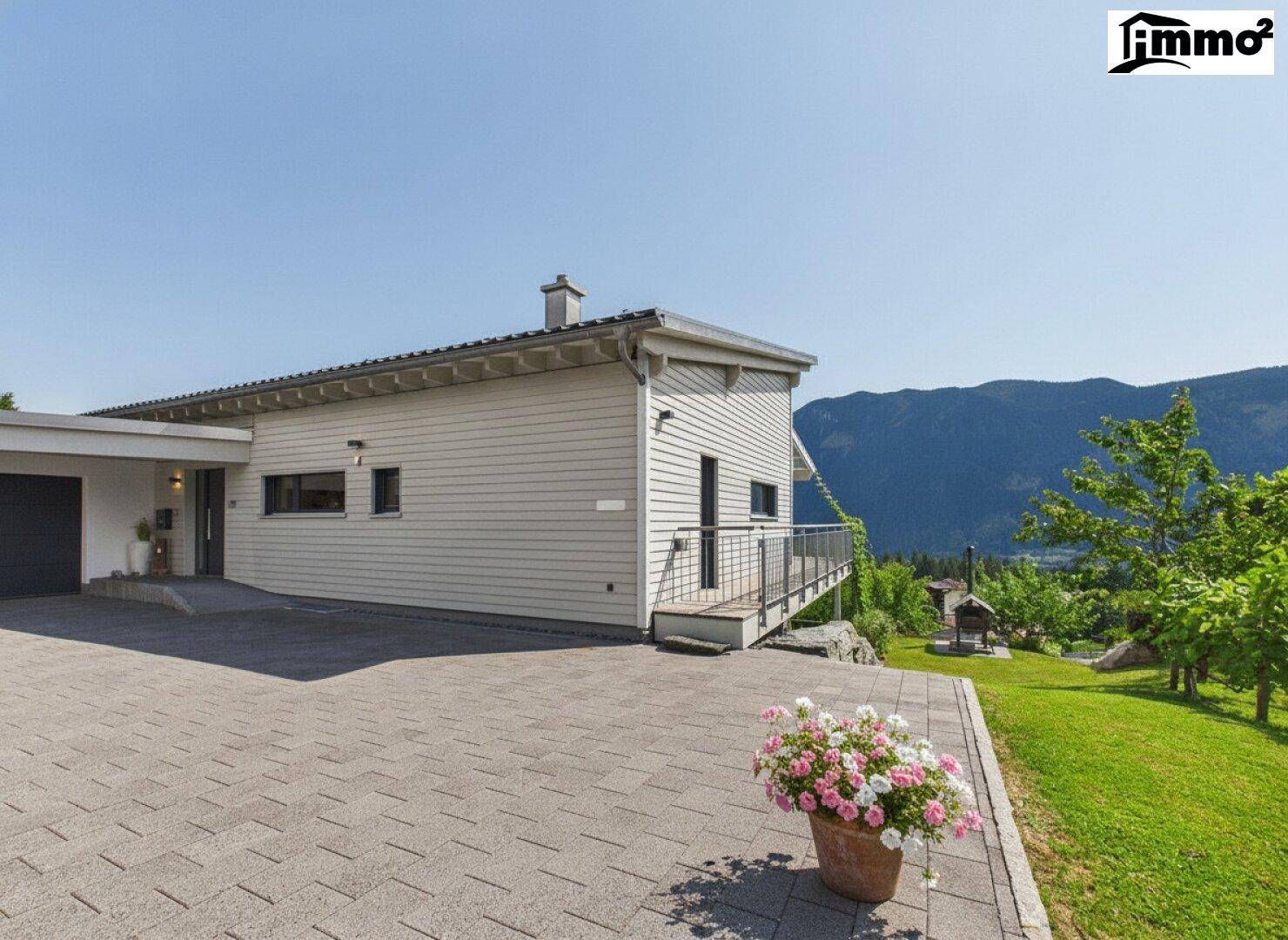Modernes Einfamilienhaus mit gepflasterter Auffahrt, Garage und Bergblick im Hintergrund.