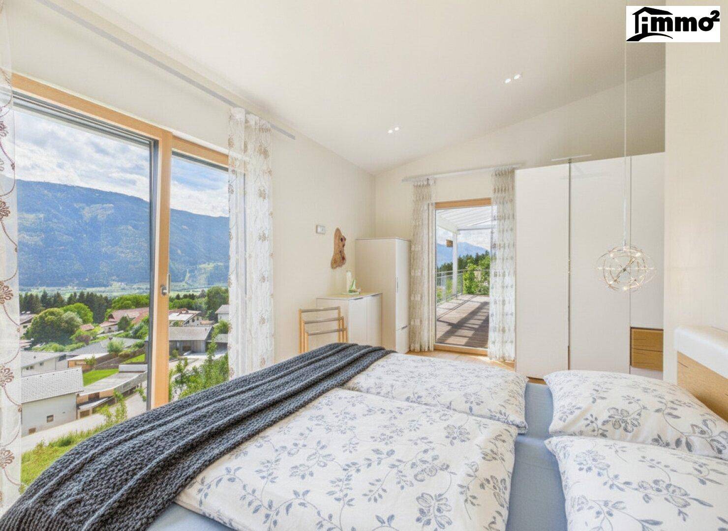Helles Schlafzimmer mit großen Fenstern, Zugang zum Balkon und Panoramablick auf die Berge.