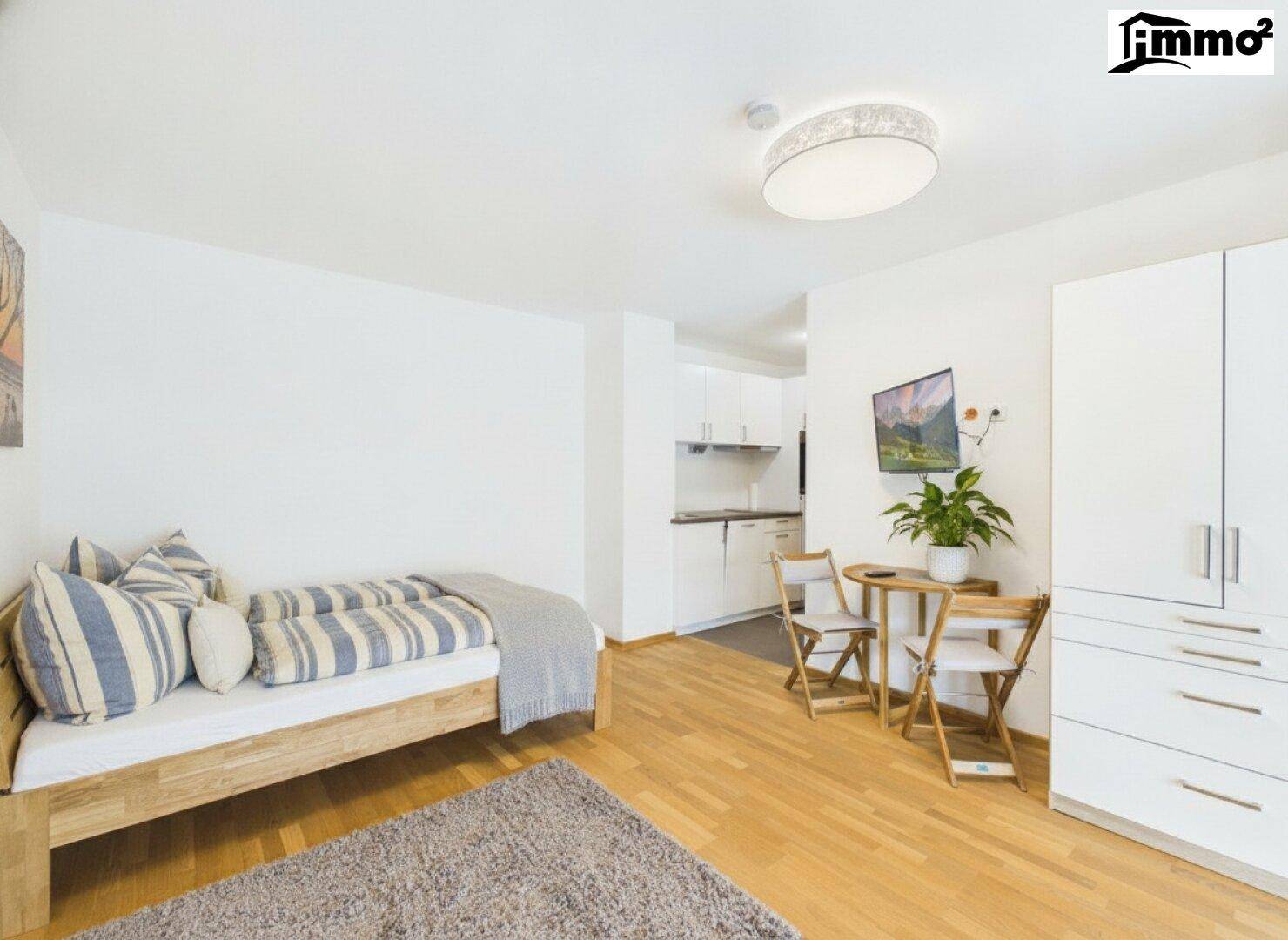 Helles Schlafzimmer mit Holzboden, integrierter Küchenzeile und modernem Mobiliar.