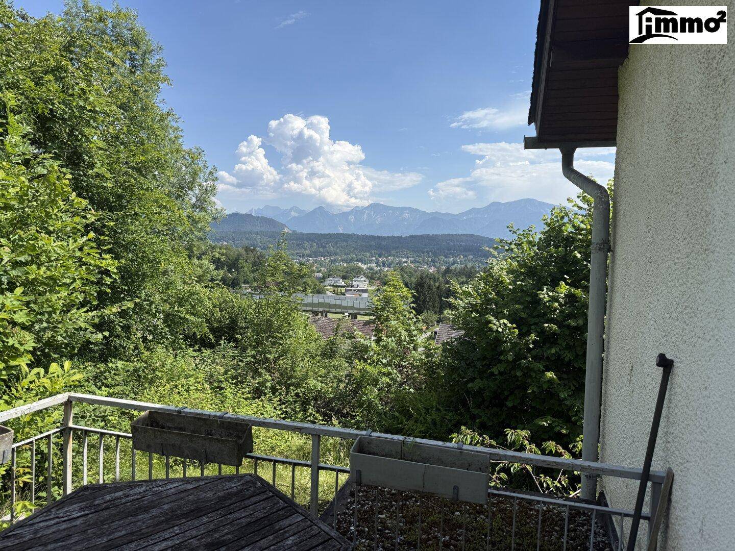 Ein Balkon mit Holztisch und einem weiten Blick über die Landschaft und Berge.