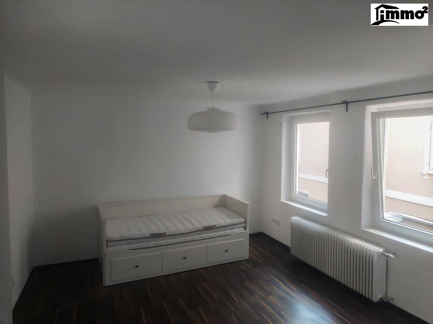 Helles Schlafzimmer mit weißem Tagesbett und dunklem Holzboden, ideal als Gäste- oder Kinderzimmer.