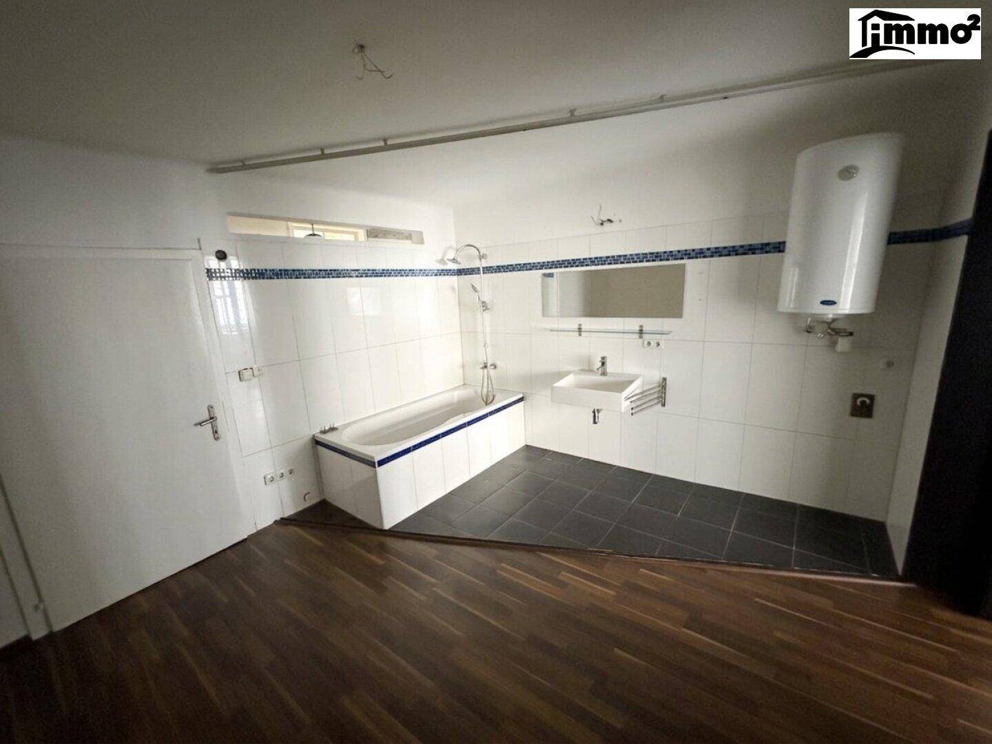 Badezimmer mit Badewanne, Waschbecken und Wandfliesen in Weiß und Blau, ausgestattet mit einem Boiler.