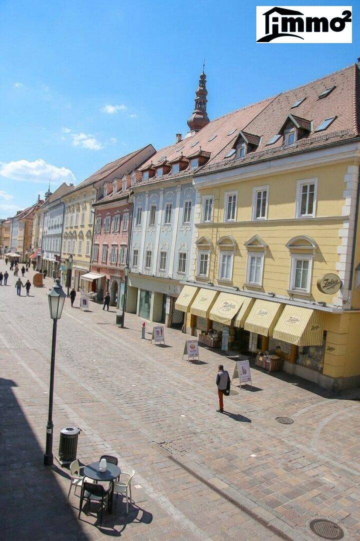 Historische Gebäude entlang einer belebten Kopfsteinpflasterstraße in der Stadt unter blauem Himmel.