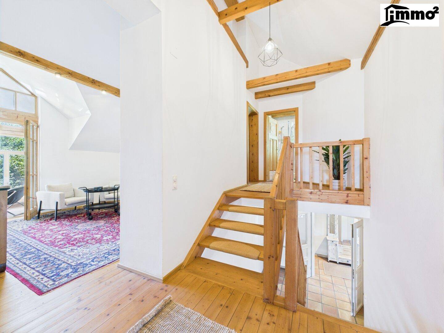 Heller Flur mit Holztreppe, Holzboden und offenem Übergang zu weiteren Räumen.