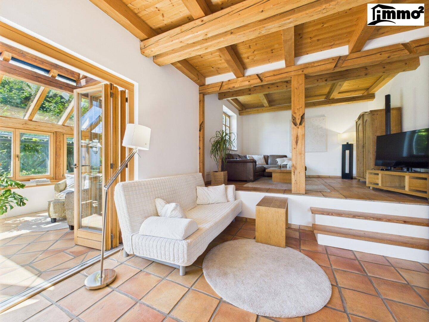 Gemütliches Wohnzimmer mit Terracotta-Boden, Holzbalken und Zugang zum Wintergarten.