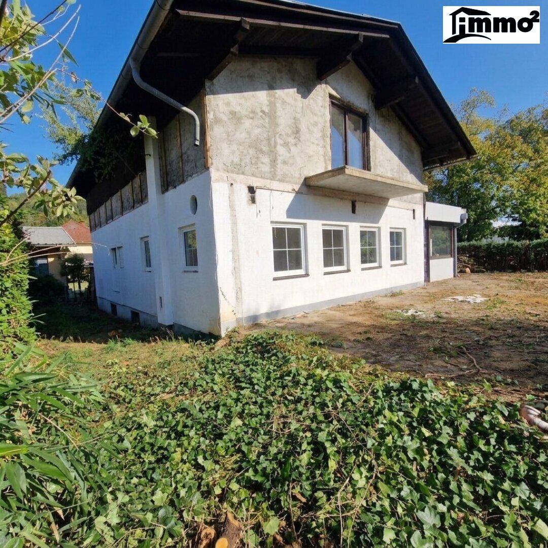 Seitenansicht des Hauses im Umbau, umgeben von dichter Vegetation.