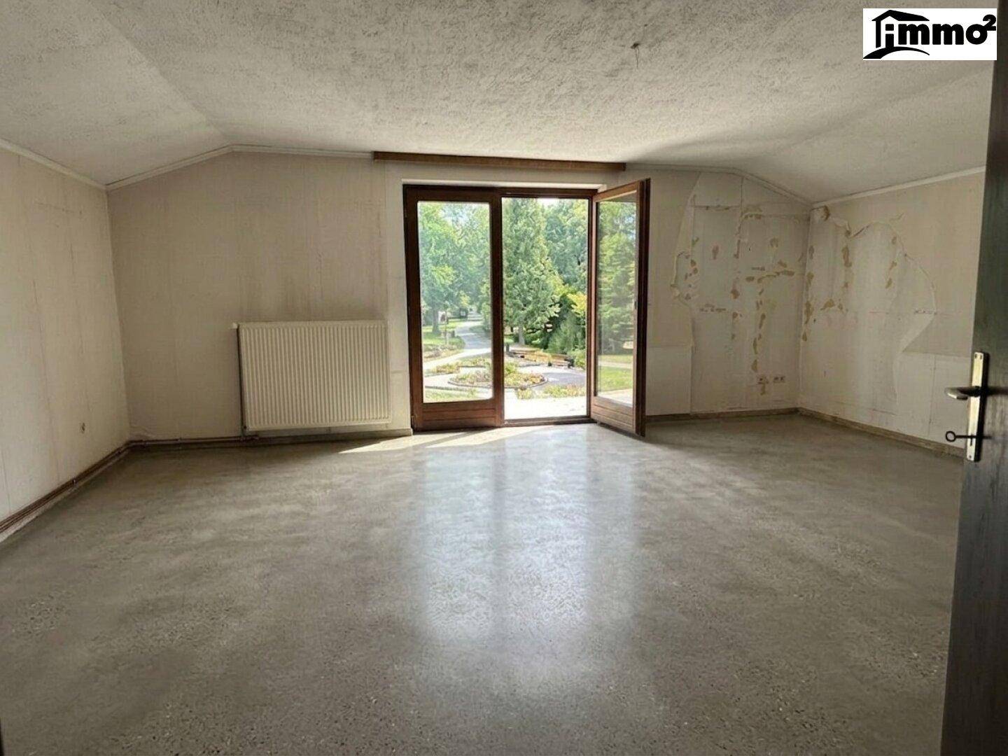 Heller Raum mit Betonboden und großen Glastüren, die Zugang zum Außenbereich bieten.