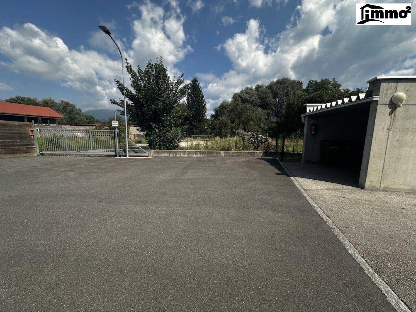 Großer asphaltierter Parkplatz mit Carport im Hintergrund.