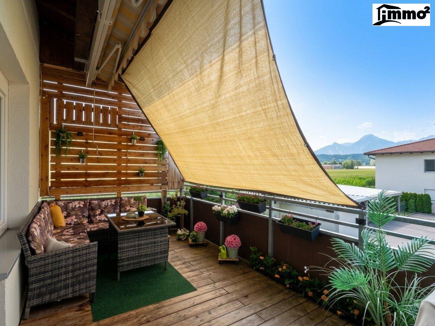 Gemütlicher Balkon mit Holzboden, Sonnensegel und weitem Blick auf die Berge.