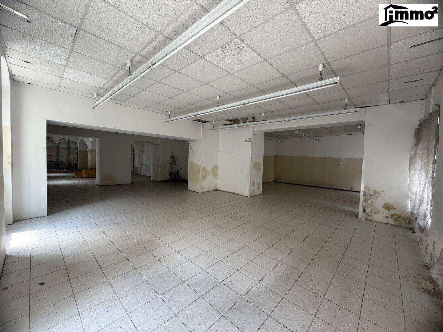Großer, leerer Raum mit Fliesenboden und abgehängter Decke, renovierungsbedürftig.