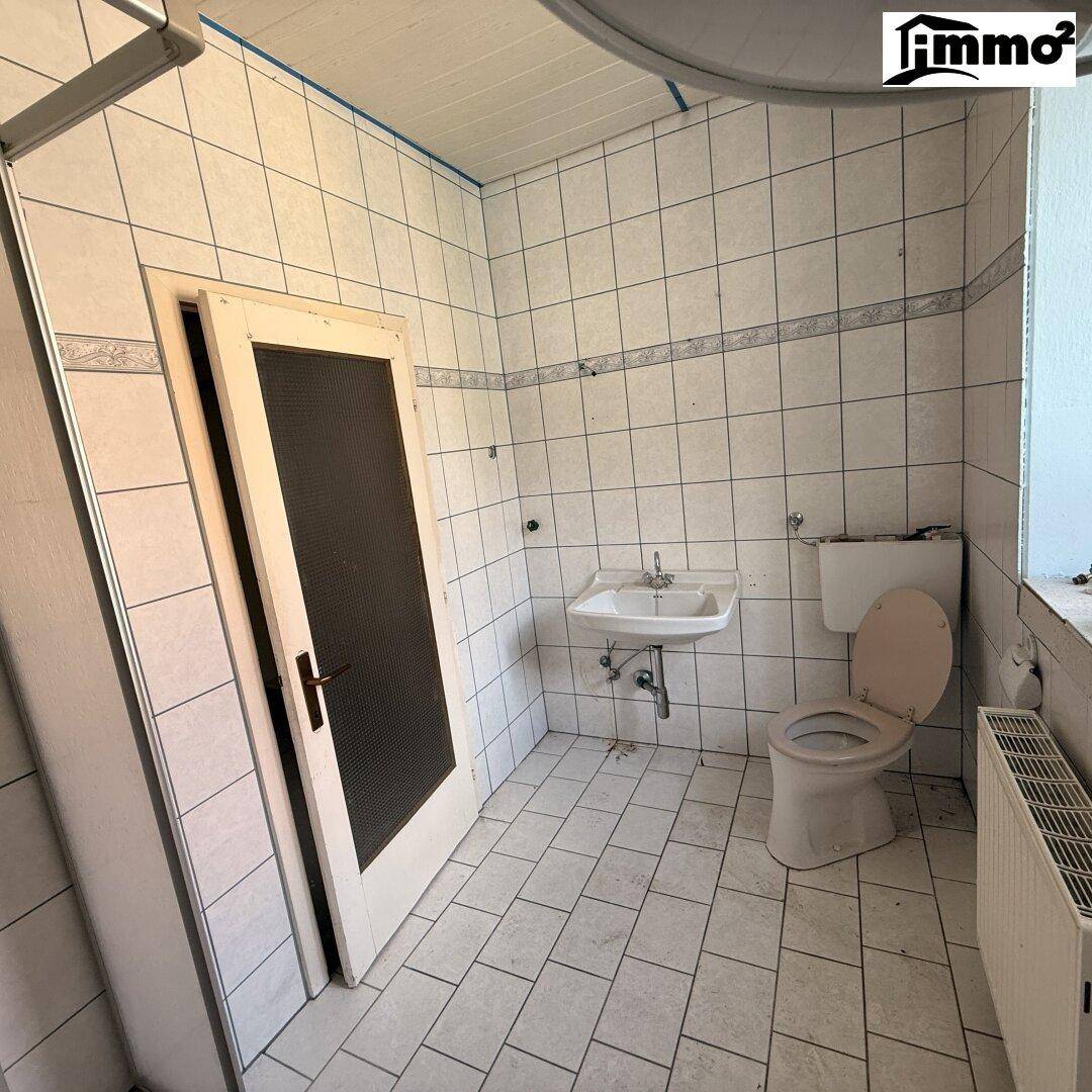 Einfaches WC mit Fliesen an Wänden und Boden, ausgestattet mit Toilette und Waschbecken.