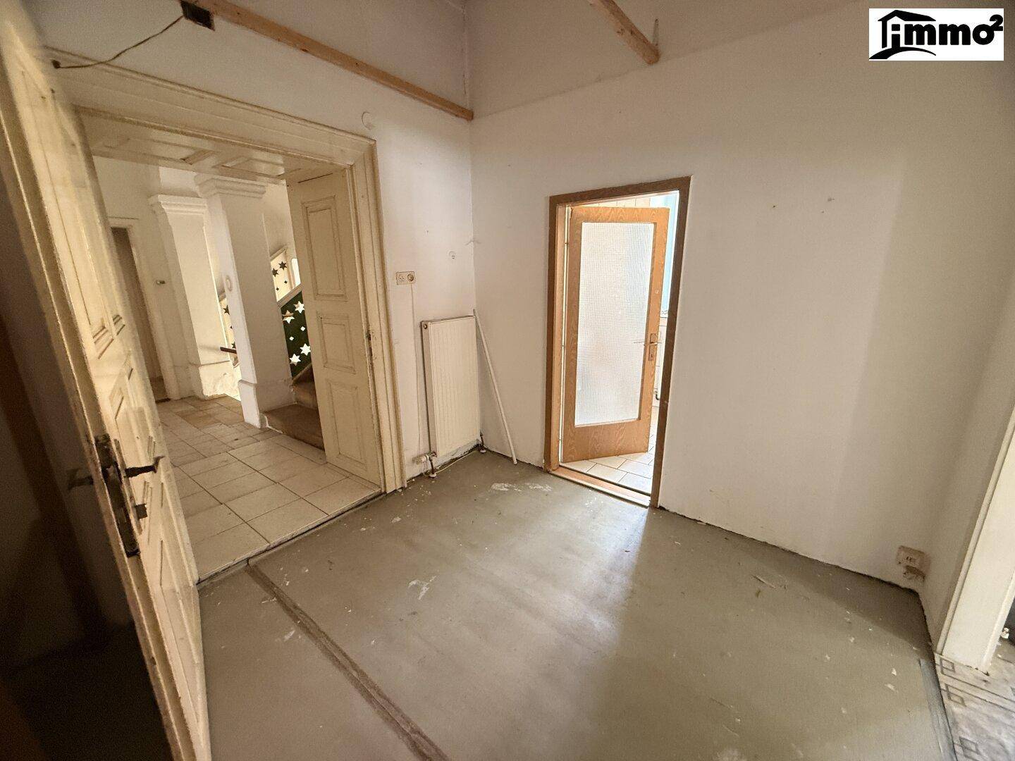 Leerer Raum mit freiliegenden Deckenbalken und einfachem Boden, bereit zur Renovierung.