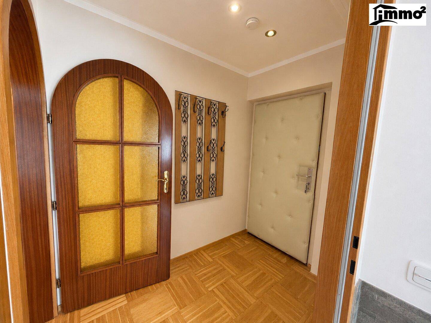 Heller Eingangsbereich mit Parkettboden, Holztüren und einer dekorativen Garderobe.