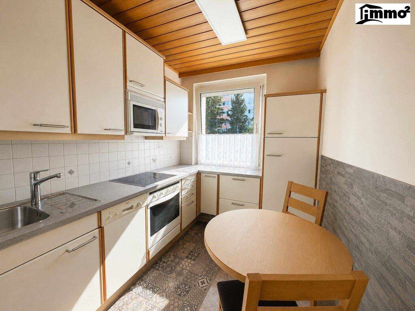 Gemütliche Küche mit weißen Einbauschränken, Holzbalkendecke und kleinem Esstisch.