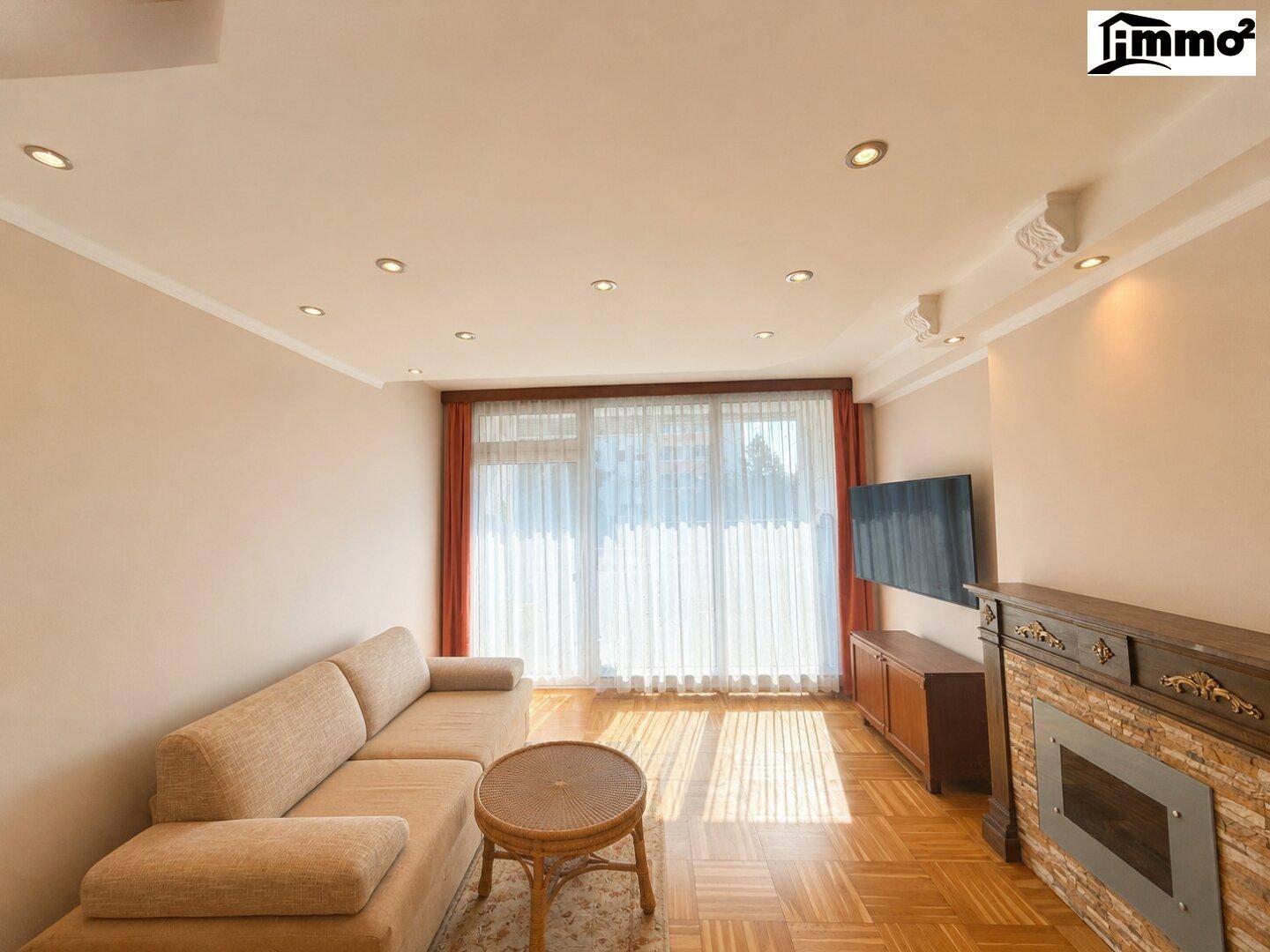 Helles Wohnzimmer mit Parkettboden, beigem Sofa, Kamin und Zugang zum Balkon.