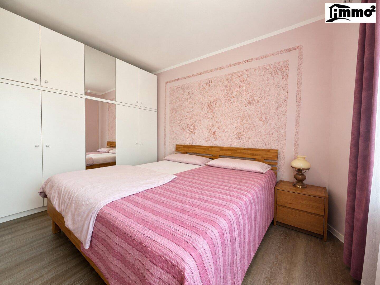 Geräumiges Schlafzimmer mit Doppelbett, Einbauschränken und rosa Akzenten.