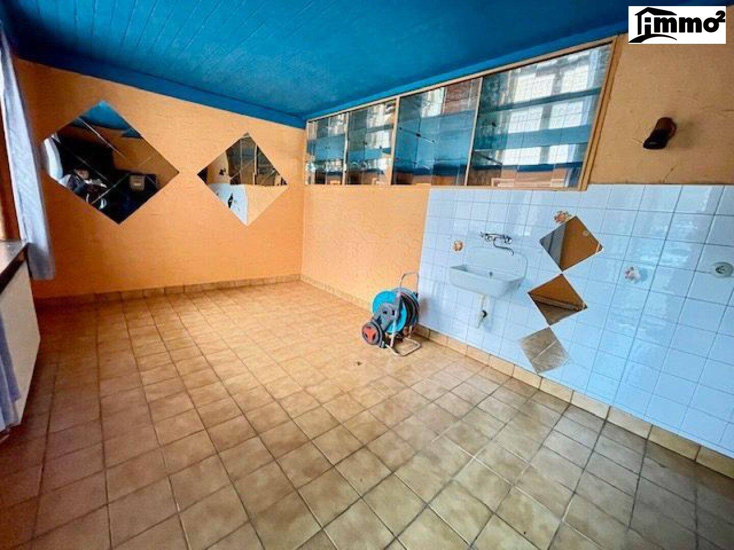 Einfacher Hauswirtschaftsraum mit Fliesenboden, Waschbecken, blauer Decke und orangefarbenen Wänden.