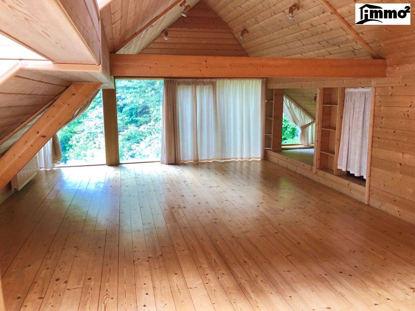 Heller, geräumiger Dachbodenraum mit Holzböden, Holzverkleidung und großen Fenstern mit Waldblick.