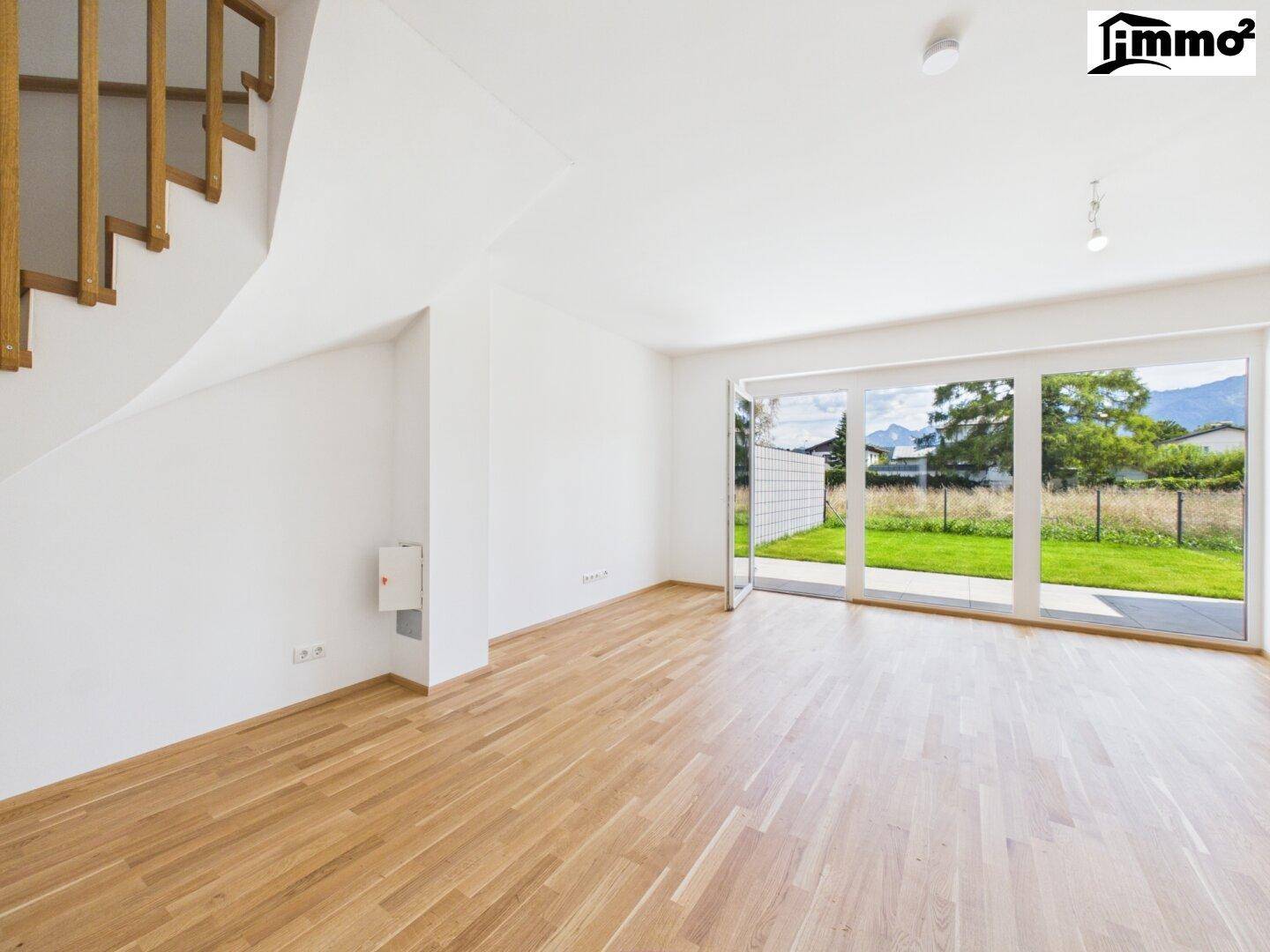 Geräumiges Wohnzimmer mit Holzboden, Treppe und großen Fenstern mit Blick auf den Garten und die Berge.