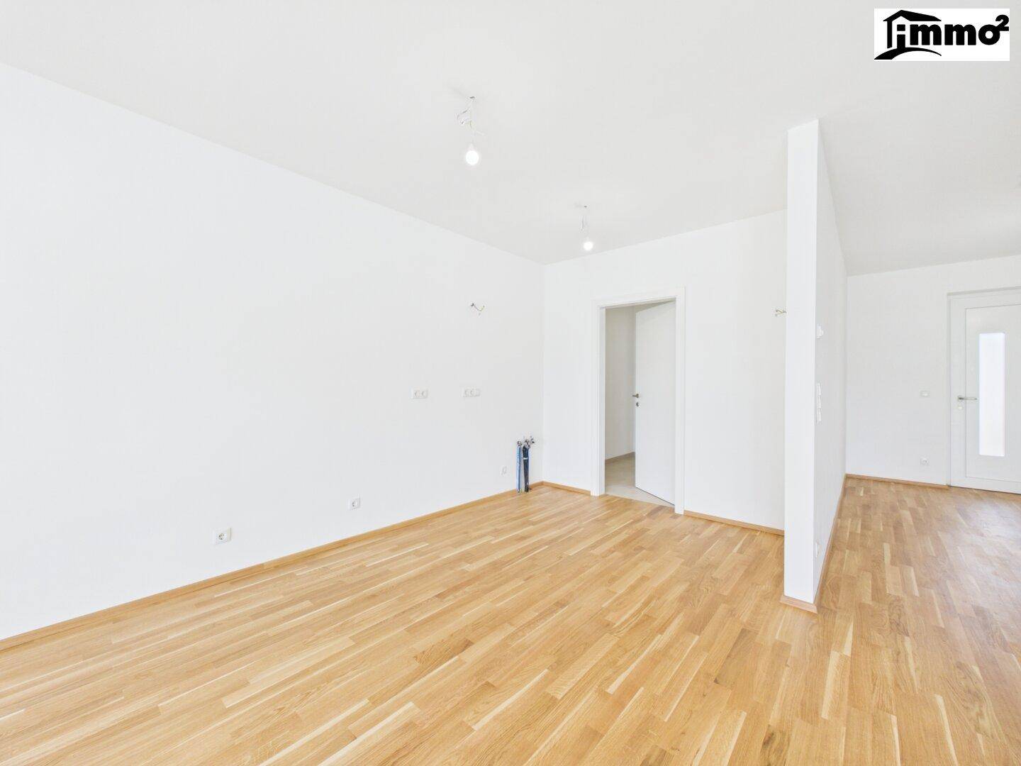 Leerer Küchenbereich mit Holzboden und vorbereiteten Anschlüssen für eine Einbauküche.