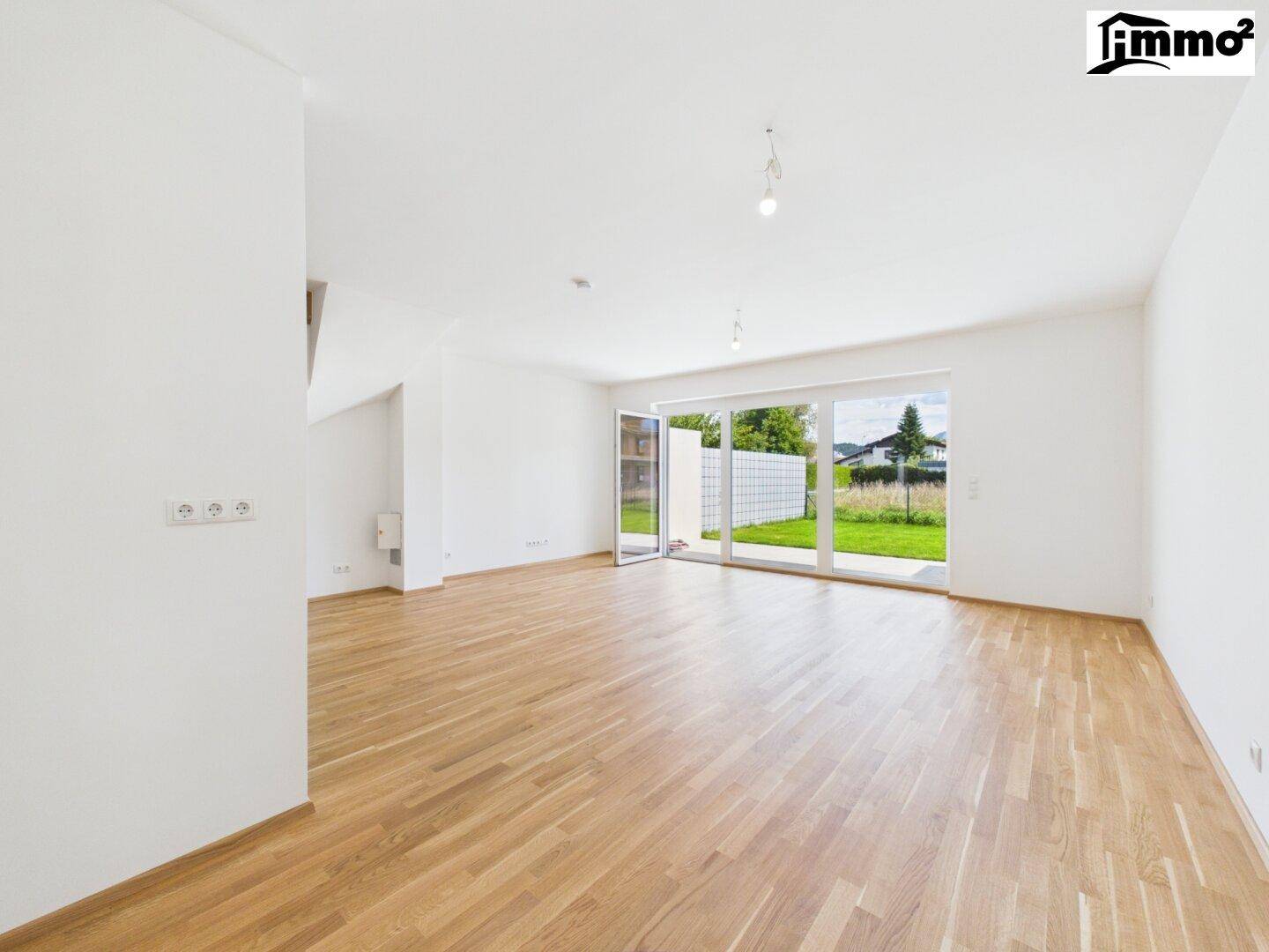 Helles Wohnzimmer mit Holzboden und großen Fenstern, die Zugang zum Garten bieten.