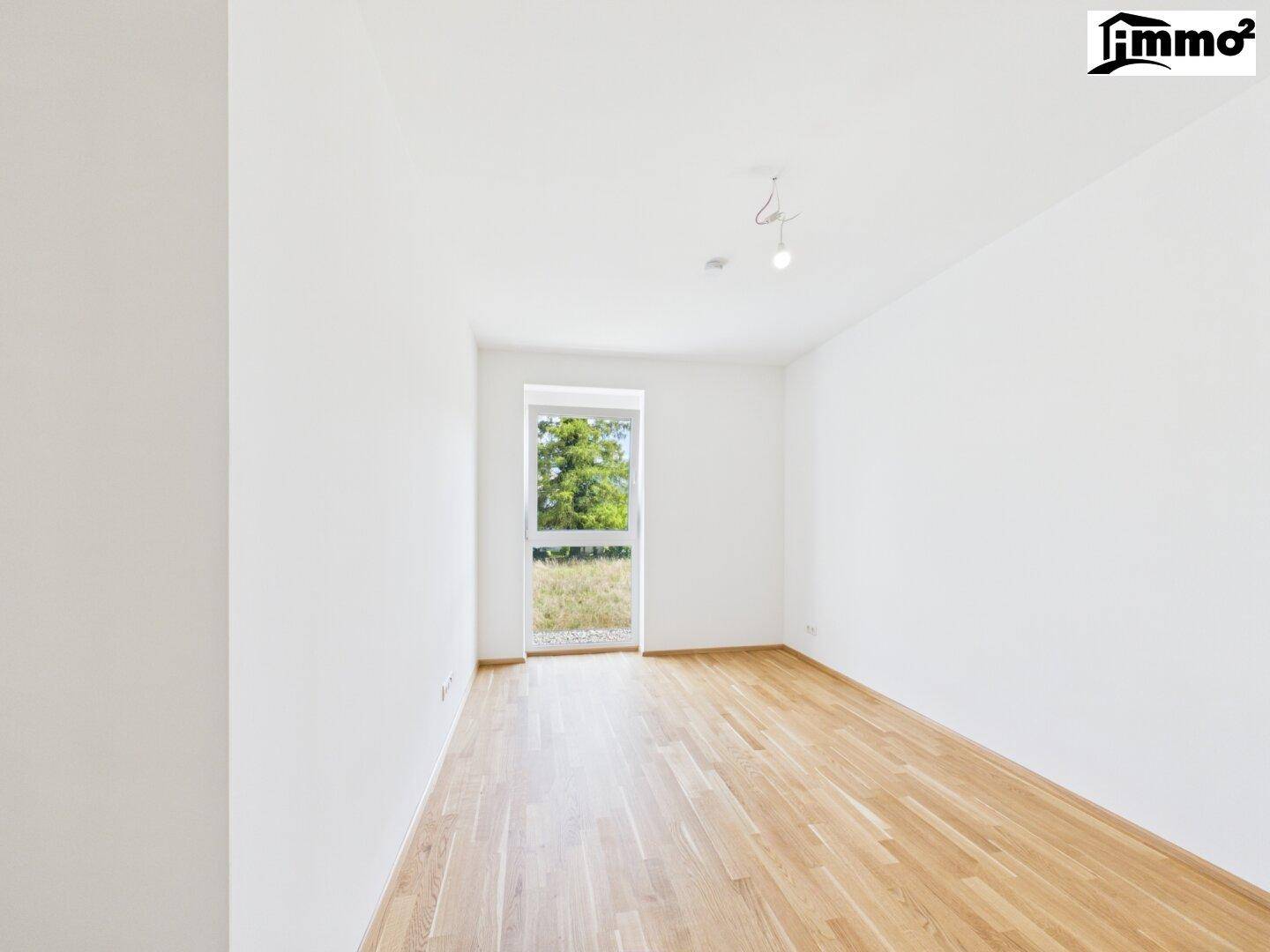 Heller, leerer Raum mit Holzboden und einem Fenster, das für ausreichend Tageslicht sorgt.
