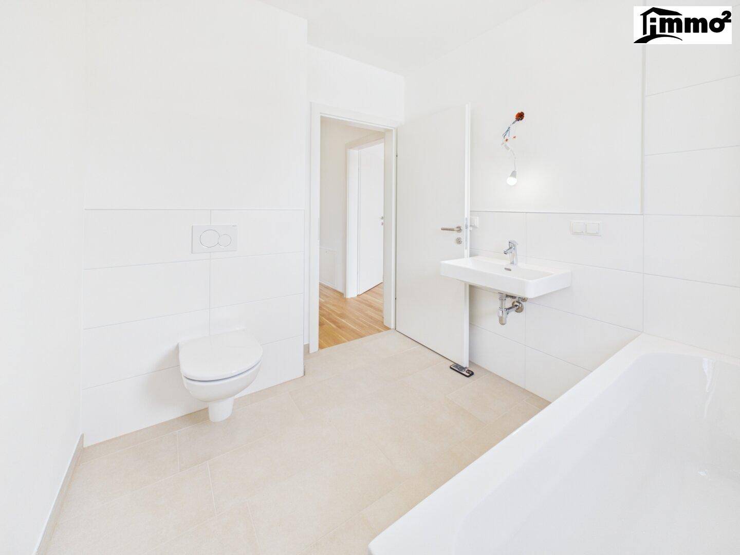 Helles Badezimmer mit Badewanne, wandhängendem WC und Waschbecken, mit Zugang zum Flur.